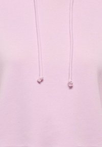 Hoodie court rose clair en tissu doux, avec une capuche à cordon aux extrémités nouées et une surface lisse et texturée.