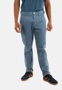 Chinos azul claro con una textura suave, que presentan un cierre con botón, pasadores para cinturón y puños doblados, combinados con zapatillas oscuras.
