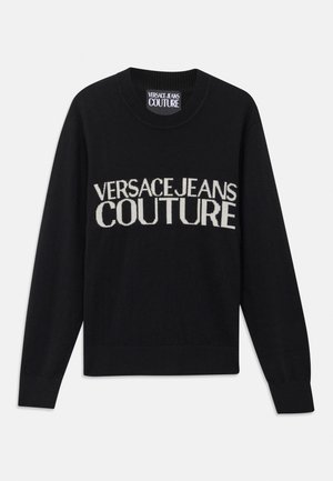 Juodas megztinis su apvaliu kaklu. Savoje sudėtyje turi kontrastingą kreminės spalvos "VERSACE JEANS COUTURE" logotipą. Raišteliuose ir apatine dalyje - gūbriška tekstūra. Minkšta tekstūra.