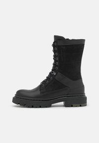 Botas negras de cuero y ante hasta el tobillo, con diseño de cordones, suela de goma gruesa y acentos texturizados.