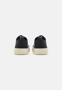 Black canvas slip-on shoes with a textured surface and a light-colored rubber sole. Minimalist design, no prominent embellishments.