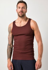 Top sin mangas burdeos hecho de tela acanalada, con un escote redondo y tirantes anchos, diseño ajustado, con un brazo tatuado visible.