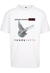 Hvid bomulds t-shirt med et grafisk motiv af en due i flugt, med teksten "upscale studios SKY" og "ready to fly" i sort og rødt.