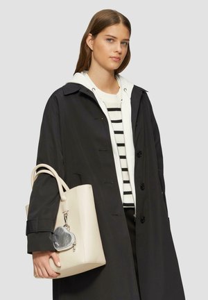 Zwarte jas met een kraag over een wit met zwart gestreept trui, gecombineerd met een lichtbeige tote bag met een hartvormige hanger.