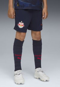 Navyfärgade shorts från Red Bull Salzburg med logotyp, navyfärgade knähöga strumpor med röd text "SOIZBURG" och vita fotbollsdojor med grå accenter.