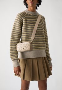 Beige schoudertas met een gestructureerd patroon, gouden hardware en een afneembare strap. Draagt bij een gestreepte trui en een geplooide rok.