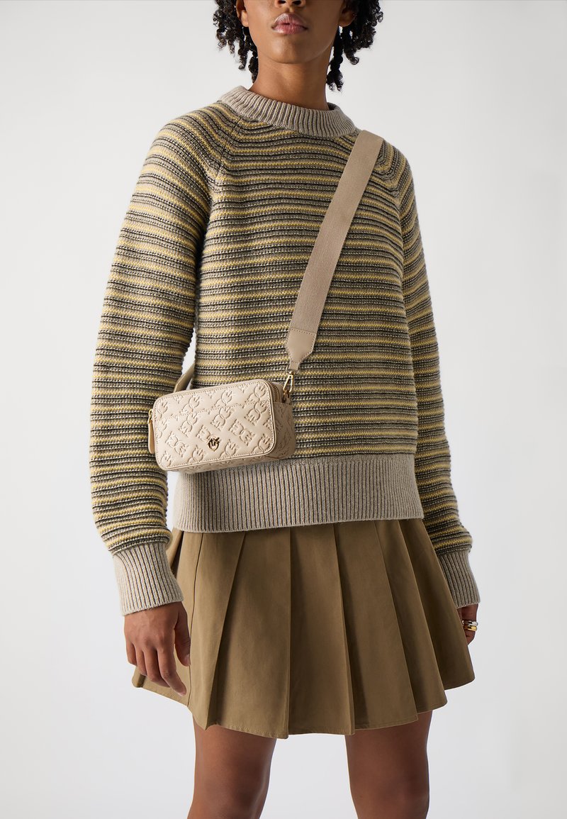 Beige schoudertas met een gestructureerd patroon, gouden hardware en een afneembare strap. Draagt bij een gestreepte trui en een geplooide rok.