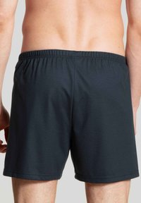 Donkerblauwe zwembroek met een elastische tailleband, met een gladde textuur en een eenvoudig ontwerp, dat net boven de bovenbenen eindigt.