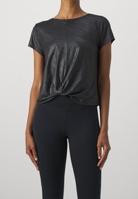 Top corto negro brillante de manga corta con un diseño frontal retorcido. Textura suave y corte relajado, combinado con leggings oscuros.
