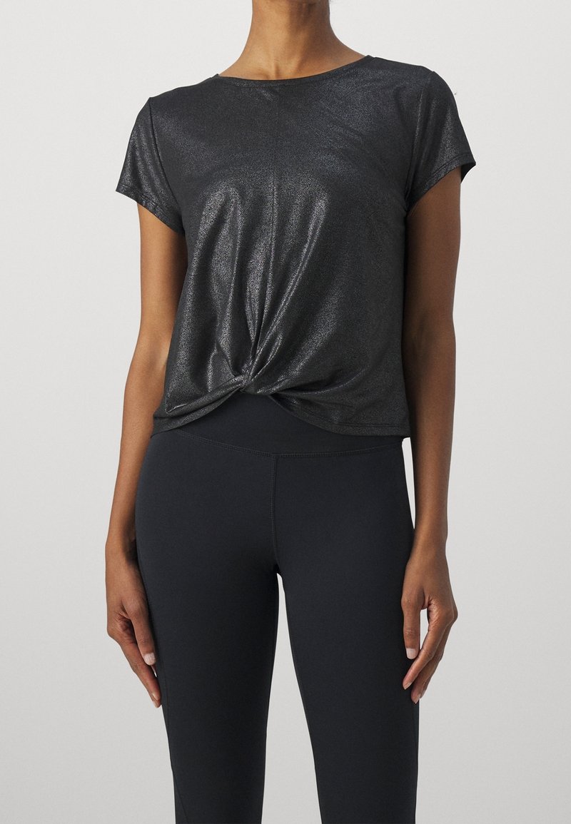 Top corto negro brillante de manga corta con un diseño frontal retorcido. Textura suave y corte relajado, combinado con leggings oscuros.