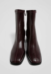 Burgundin nahka nilkkurit, joissa on neliön muotoinen kärki, erottuva punainen tikkaus ja sivuvetoketju helppoa pukemista varten. Tasainen musta pohja.