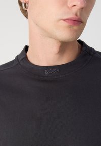 Camiseta negra ligera de cuello redondo, hecha de algodón; cuenta con una sutil etiqueta del logo "BOSS" cosida en el cuello. Textura suave, diseño ajustado.