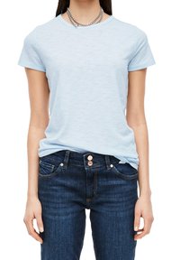 Vaaleansininen puuvillapaita, jossa on lyhyet hihat, pyöreä pääntie ja pehmeä pinta; yhdistetty tummansinisiin farkkuihin, joissa on kuparinväriset nappikoristeet.