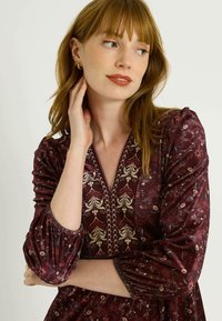 Vestido burdeos con estampado floral, escote en V y bordados decorativos. Manga larga abullonada con puños elásticos para un efecto fruncido.