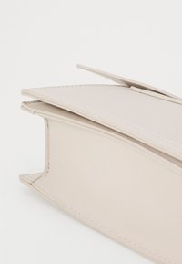 Portefeuille beige en matériau synthétique lisse, présentant une forme rectangulaire avec des bords angulaires et des coutures visibles le long des seams.