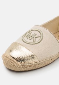Chaussure espadrille en tissu beige avec embout métallique doré et logo MK brodé sur la tige, semelle en jute tressée.