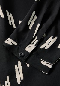 Tessuto nero con motivo bianco irregolare, dotato di polsino con bottoni e superficie liscia. Il design mette in evidenza il contrasto tra i colori.