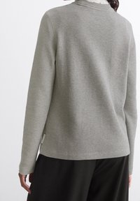 Maglione grigio con texture, collo a giro e maniche lunghe, caratterizzato da un motivo a coste. L'orlo inferiore è leggermente più lungo sul retro.