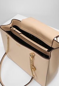 Béžová kožená kabelka s pevnou strukturou, obsahující horní zipovou přihrádku, zlaté řetízkové detaily a vzorovanou podšívku.