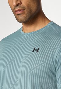 Camiseta atlética de manga corta hecha de una tela ligera azul texturizada. Presenta un logo negro en el lado izquierdo del pecho y un sutil patrón de rayas diagonales.