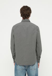 Fekete-fehér kockás ing könnyű anyagból, gallérral, hosszú ujjakkal és ívelt szegéllyel. A hátsó nézet gombos mandzsettákat mutat.