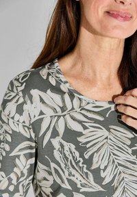 Grijze stoffen top met een bloemenpatroon in het wit, met een ronde halslijn en een zachte textuur, die bladeren en botanische ontwerpen accentueert.