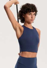 Tengerészkék sport crop top, kerek nyakkivágással és ujjatlan kialakítással, sima anyagból készült. Feszes vonalvezetés és texturált oldalsó részletek jellemzik.