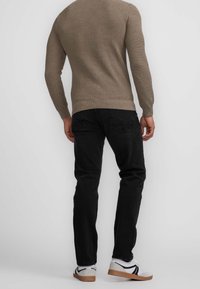 Hellbrauner Strickpullover, schwarze Jeans und weiße Sneaker mit schwarzen Akzenten, die eine gerippte Textur und kontrastierende Materialien zeigen.
