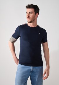 Camiseta ajustada de color azul marino, hecha de algodón, con mangas cortas y franjas blancas y rojas a lo largo de los hombros, y un pequeño logo en el pecho.