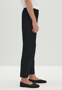 Svarta skräddarsydda byxor med en slät textur, smal passform, sidofickor och en liten dragkedjedetalj vid fållen, kombinerade med svarta platta skor.