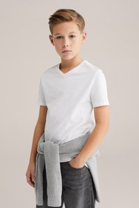 Balti V formos kaklo marškinėliai derinami su tamsiomis džinsomis ir šviesiai pilku megztiniu, užrištu aplink liemenį. Minimalistinis dizainas ir neutralių spalvų derinys.