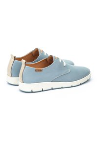 Zapatillas azul claro hechas de cuero texturizado, con una suela blanca, acentos beige y cordones planos. Logo de la marca visible en el lado.