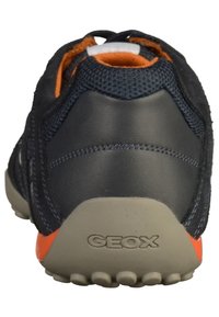 Bakåtsyn av en svart och orange Geox-sneaker med texturerad häl och synlig bröllogo på beigesula.