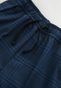 Shorts en tartan marine fabriqués dans un tissu doux, dotés d'une taille à cordon de serrage et d'accents noirs. Le motif comprend des lignes bleues et bleu marine.
