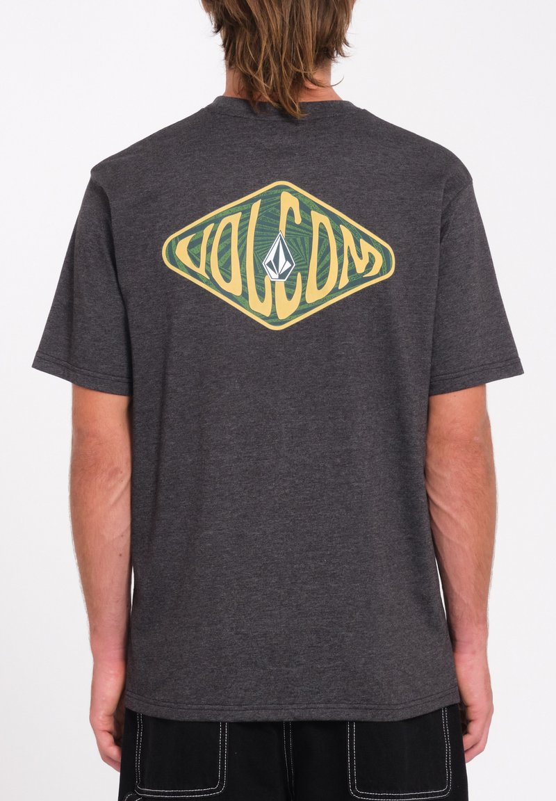 T-shirt en coton gris avec un grand logo en forme de diamant jaune et vert au dos, avec un emblème triangulaire au centre. Manches courtes.