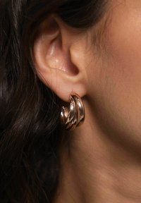 Ohrringe aus Roségold mit einem strukturierten, gedrehten Design. Glatte, reflektierende Oberfläche mit einer modernen und skulpturalen Form.