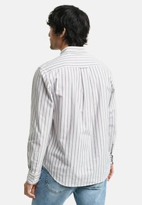 Koszula z długim rękawem, zapinana na guziki, wykonana z lekkiego materiału z pionowymi paskami w kolorze niebieskim, czerwonym i białym. Ma plisy z tyłu oraz zaokrąglony dół.