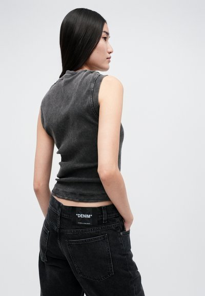 Pelēks bez piedurknēm topiņš no džinsa, pieguļošs dizains ar ribotu tekstūru; apvienots ar tumšā džinsa biksēm ar redzamu "DENIM" etiketīti.