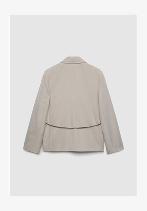 Blazer beige chiaro con design su misura, caratterizzato da uno spacco singolo sul retro, bavero affilato e una texture liscia e opaca.