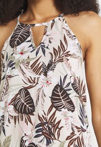 Bluzka w kwiatowy wzór z kremowym tłem, brązowymi i zielonymi liśćmi oraz detalem w kształcie dziurki na szyi. Lekka tkanina o gładkiej fakturze.