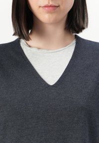 Maglione grigio scuro a scollo a V sovrapposto a una camicia grigio chiaro. Tessuto morbido con una texture liscia e un design casual. Scollo distintivo.