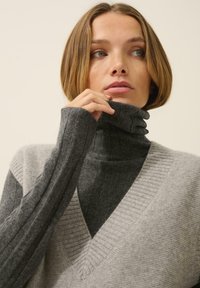 Szary i węglowy sweter z golfem w kształcie litery V, z prążkowaną fakturą i warstwowym wyglądem. Miękka dzianina.