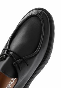 Zapato de cuero negro con una textura suave, punta redonda y acentos cosidos. Presenta un diseño con cordones y una suela de goma minimalista.