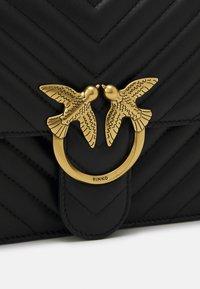 Zwarte leren handtas met chevron-stiksel en een gouden vogelvormige sluiting. Bevat een ronde hardwareaccent en een gestructureerd oppervlak.