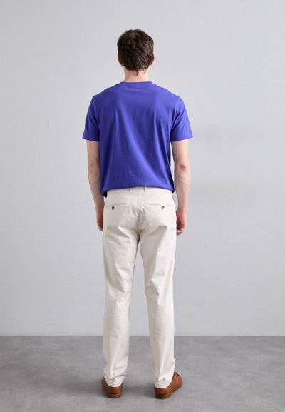 Purple short-sleeve shirt, light-colored pants, brown shoes. Visible stitching on pants, no patterns. Neutral background with gray flooring.