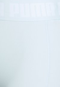 Jasnoniebieskie legginsy sportowe z szerokim, białym pasem z logo oraz gładką, elastyczną fakturą materiału, z płaskimi szwami dla komfortu.