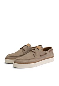 Zapatos de ante beige con cordones, detalles perforados, cordones marrones y suela de goma blanca. Presentan un diseño cosido y un logo sutil en el lateral.