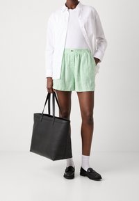 Zielono-białe spodenki w paski z elastycznym pasem, noszone z białym t-shirtem i długim białym rękawem; trzymające czarną skórzaną torbę.