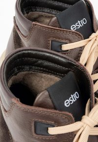 Bruineleren enkelboots met beige veters, een gevoerde kraag en subtiele stiksels. Voorzien van een zwart stoffen label met het "estro" logo aan de binnenzijde.