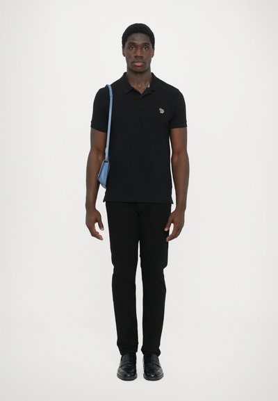 Black polo shirt with a small logo, paired with black pants and black shoes. A light blue shoulder bag is worn across the body.